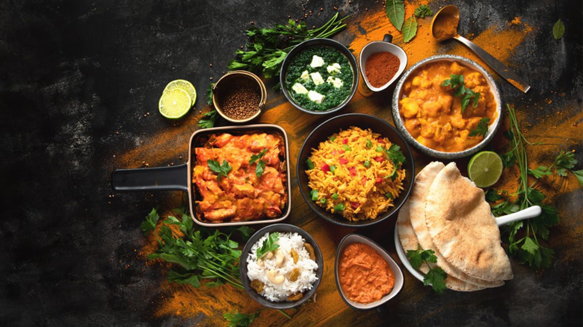 A vibrant spread of Indian dishes including breads biryani curries and chutneys arranged in a rustic table with fresh herbs and spices