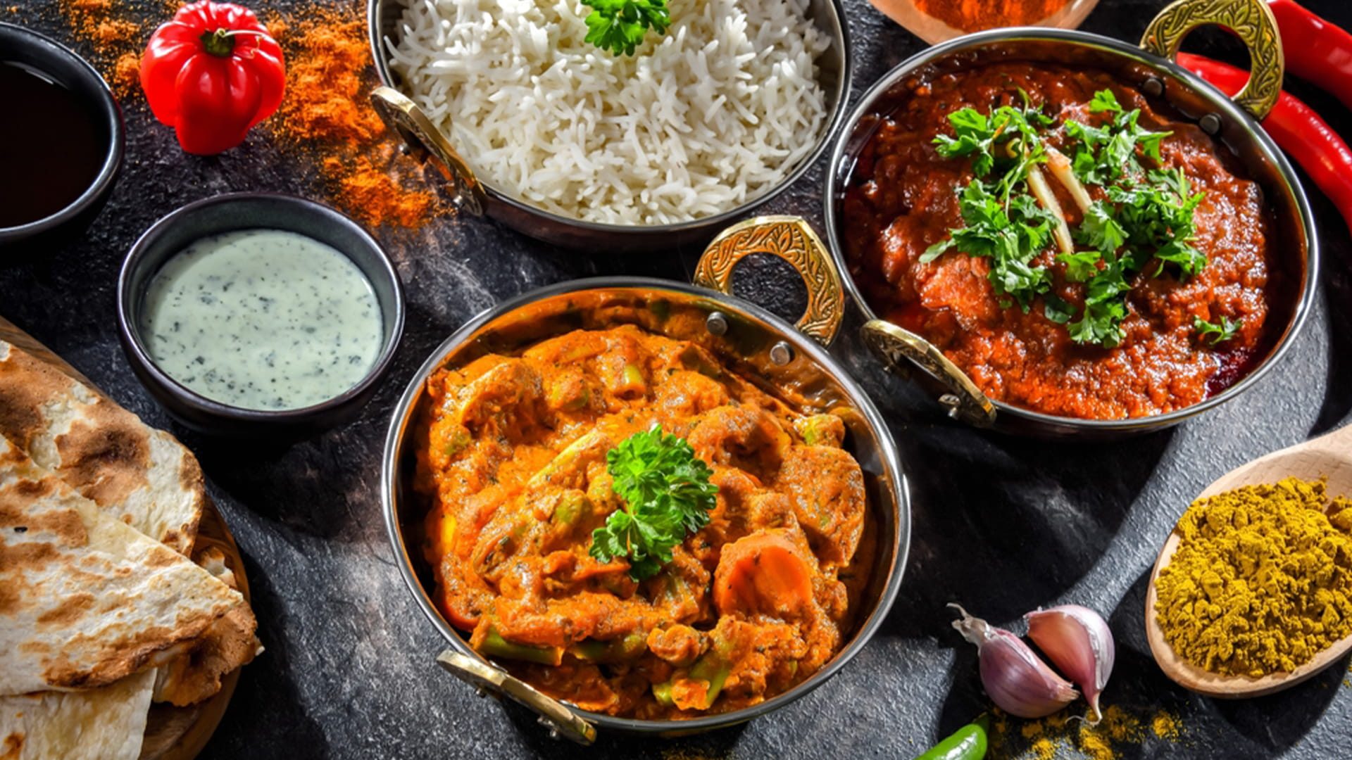 Close-up of assorted Indian curries, rice and masala powder served in traditional bowls with fresh herbs and spices.